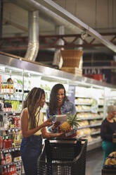 Frauen mit Einkaufsliste und Smartphone beim Einkaufen im Supermarkt - CAIF27446