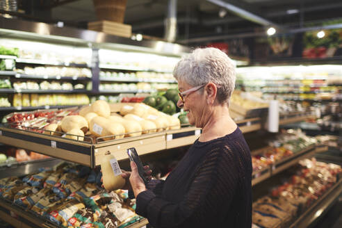 Ältere Frau mit Smartphone beim Einkaufen in der Lebensmittelabteilung eines Supermarkts - CAIF27455