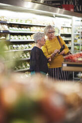 Ältere Frauen mit Smartphone beim Lebensmitteleinkauf im Supermarkt - CAIF27464