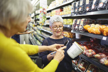 Ältere Frauen mit Smartphone beim Lebensmitteleinkauf im Supermarkt - CAIF27467