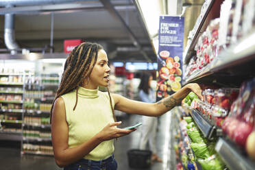 Frau mit Smartphone beim Lebensmitteleinkauf im Supermarkt - CAIF27470