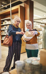 Ältere Frauen mit Smartphone beim Einkaufen in einem Haushaltswarengeschäft - CAIF27490