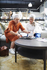 Ältere Frauen betrachten Stoffmuster in einem Möbelhaus - CAIF27497
