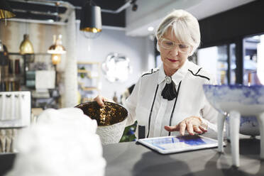 Ältere Frau mit digitalem Tablet beim Einkaufen in einem Haushaltswarengeschäft - CAIF27498
