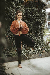 Frau übt Yoga vor einer Mauer mit Efeu - DAWF01397