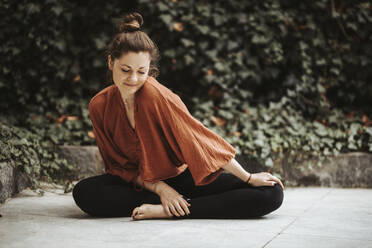 Frau übt Yoga vor einer Mauer mit Efeu - DAWF01400