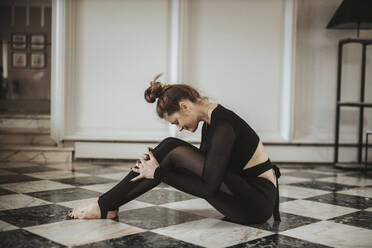 Frau übt Yoga auf schwarzem und weißem Boden zu Hause - DAWF01409