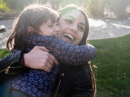 Porträt eines glücklichen kleinen Mädchens, das seine Mutter im Freien umarmt - EGAF00051