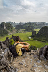 Vietnam, Provinz Ninh Binh, Ninh Binh, Männlicher Wanderer bewundert die malerische Landschaft des Hong River Deltas von der Spitze einer Karstformation aus - MAUF03386