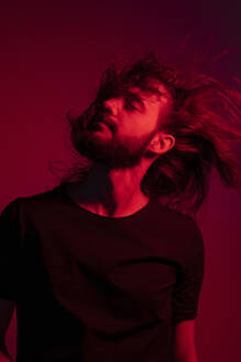 Portrait of red illuminated young man against red background tossing his hair - EGAF00053