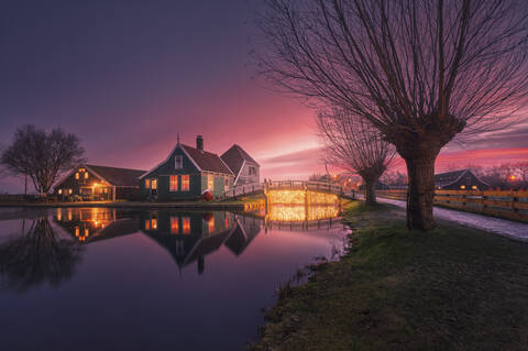 Niederlande, Nordholland, Zaanse Schans, Häuser am Flussufer bei violetter Dämmerung, lizenzfreies Stockfoto