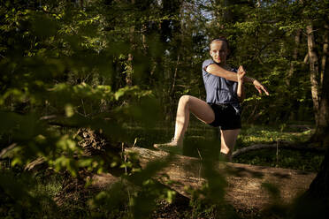 Mädchen in voller Länge mit ausgestrecktem Arm an einem umgestürzten Baum im Wald - AUF00388