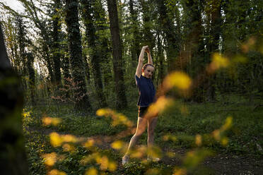 Full length of girl stretching with arms raised in forest - AUF00395