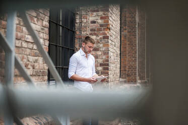 Junger Geschäftsmann mit Tablet an einem Backsteingebäude - DIGF10419