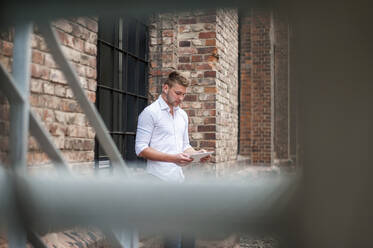 Young businessman using tablet at a brick building - DIGF10419