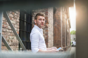 Young businessman using tablet at a brick building - DIGF10420