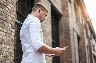 Young businessman using tablet at a brick building - DIGF10421