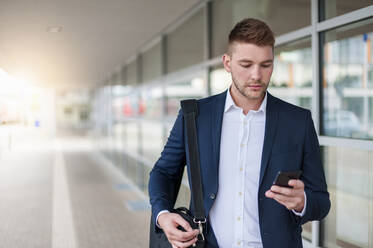 Portrait of a young businessman in the city checking his smartphone - DIGF10435