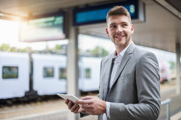 Lächelnder junger Geschäftsmann mit Tablet am Bahnhof - DIGF10443