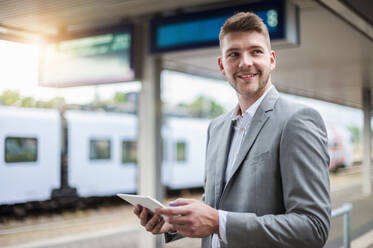 Smiling young businessman using tablet at the train station - DIGF10443