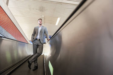 Junger Geschäftsmann auf Rolltreppe im Bahnhof - DIGF10448