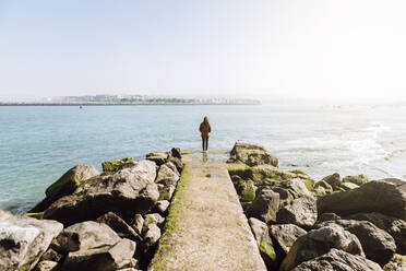 Rückansicht einer Frau in voller Länge, die auf einem Pier steht und auf das Meer gegen den klaren Himmel eines sonnigen Tages blickt - XLGF00145