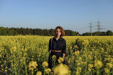 Portrait of teenage girl standing in rape field - OGF00388