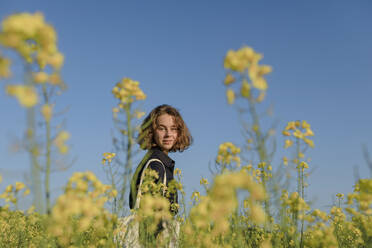 Portrait of smiling teenage girl standing in rape field - OGF00389