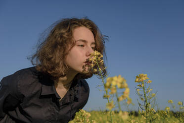 Porträt eines Teenagers, der an einer Blüte im Rapsfeld riecht - OGF00390