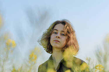 Portrait of teenage girl in rape field against sky - OGF00391