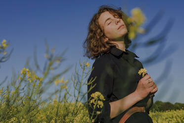 Porträt eines Teenagers mit geschlossenen Augen im Rapsfeld stehend - OGF00392