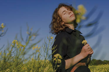 Portrait of teenage girl with eyes closed standing in rape field - OGF00392