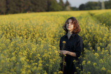 Portrait of teenage girl standing in rape field - OGF00397