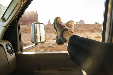 Tiefschnitt einer Frau, die sich mit hochgelegten Füßen auf einem Fahrzeugfenster entspannt, Monument Valley Tribal Park, Utah, USA - DGOF00978