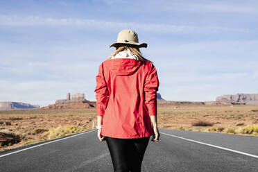 Rückansicht eines weiblichen Touristen, der auf einer Wüstenstraße läuft, Monument Valley Tribal Park, Utah, USA - DGOF00979