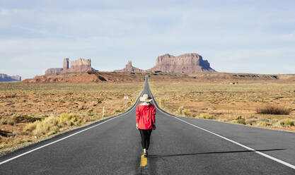 Rückansicht in voller Länge einer weiblichen Touristin, die auf einer Wüstenstraße läuft, Monument Valley Tribal Park, Utah, USA - DGOF00980