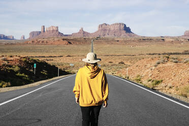 Rückansicht einer Frau, die auf einer Wüstenstraße läuft, Monument Valley Tribal Park, Utah, USA - DGOF00982