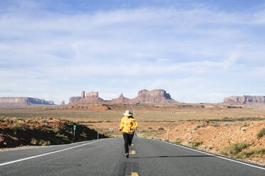 Frau läuft in voller Länge auf Wüstenstraße gegen Himmel, Monument Valley Tribal Park, Utah, USA - DGOF00983