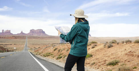Weibliche Touristin, die am Straßenrand stehend vor dem Himmel eine Karte liest, Monument Valley Tribal Park, Utah, USA - DGOF00987