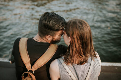 Rückansicht eines zärtlichen jungen Paares, das am Flussufer sitzt - VBF00012