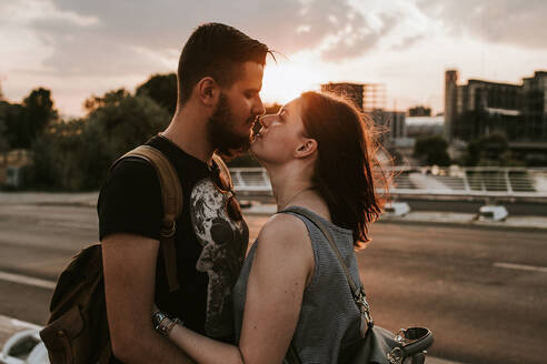 Zärtliches junges Paar umarmt sich auf einer Straße bei Sonnenuntergang, Berlin, Deutschland - VBF00025