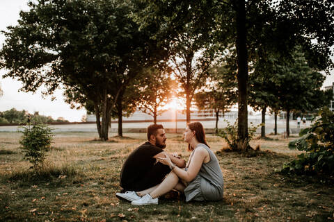 Young couple sitting in a park at sunset stock photo