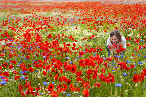 Frau riecht an frischen Blumen auf rotem Mohnfeld, lizenzfreies Stockfoto