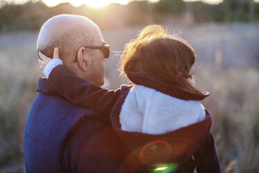 Rear view of mature man with granddaughter at countryside during sunset - EGAF00060