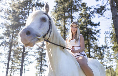 Niedriger Blickwinkel auf junge Frau reitet weißes Pferd im Wald - SNF00103