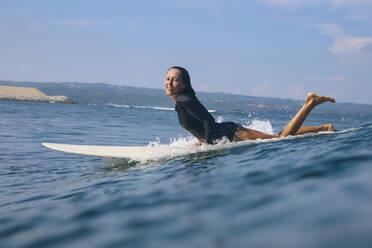 Glückliche Frau auf einem Surfbrett im Meer liegend, Bali, Indonesien - KNTF04592