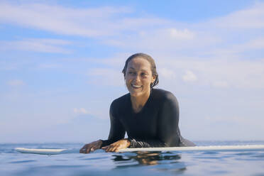 Porträt einer glücklichen Frau, die auf einem Surfbrett im Meer liegt, Bali, Indonesien - KNTF04593