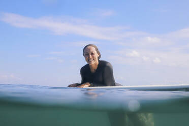 Porträt einer glücklichen Frau, die auf einem Surfbrett im Meer liegt, Bali, Indonesien - KNTF04594