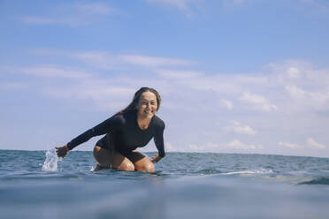 Porträt einer glücklichen Frau, die auf einem Surfbrett im Meer kniet, Bali, Indonesien - KNTF04597