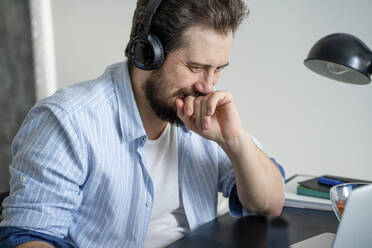 Mann mit Laptop und Kopfhörern bei der Arbeit zu Hause - VPIF02423